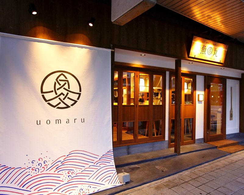 uomaru の暖簾と「鮮魚と炉端焼き 魚丸」の行灯看板が灯る、魚丸 彦根店の外観（彦根市旭町）