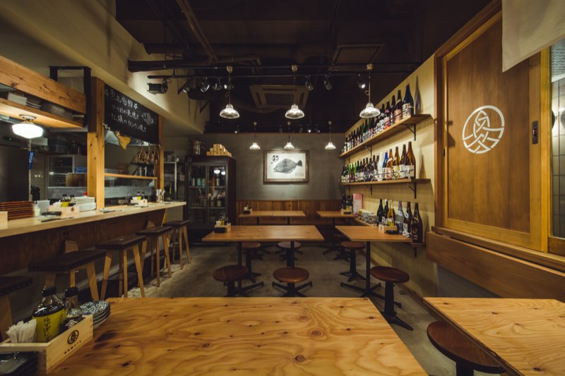 カウンターとテーブル席が並ぶ魚丸 南草津店の店内。奥の棚に日本酒の瓶、壁に魚拓の額