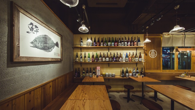 三段の棚に日本酒の瓶がずらりと並ぶ魚丸 南草津店の店内。左手に「鮮」の魚拓額