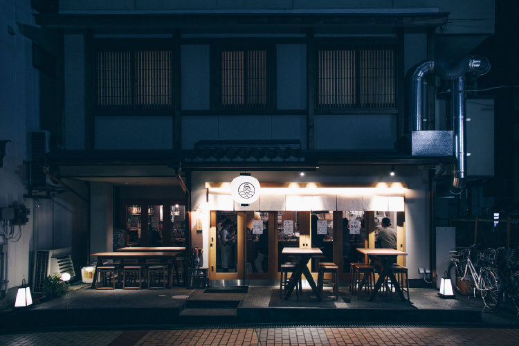 白提灯が灯る夜の店舗外観。軒下にテラス席（炉端と日本酒 魚丸 守山店）