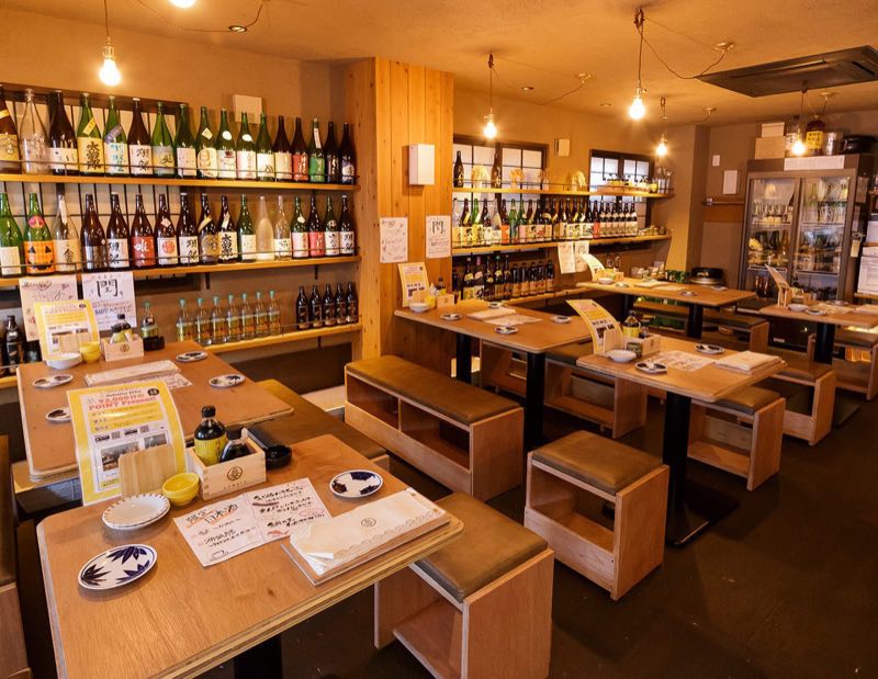 壁一面に日本酒の一升瓶が並ぶ1階のテーブル席（炉端と日本酒 魚丸 守山店）